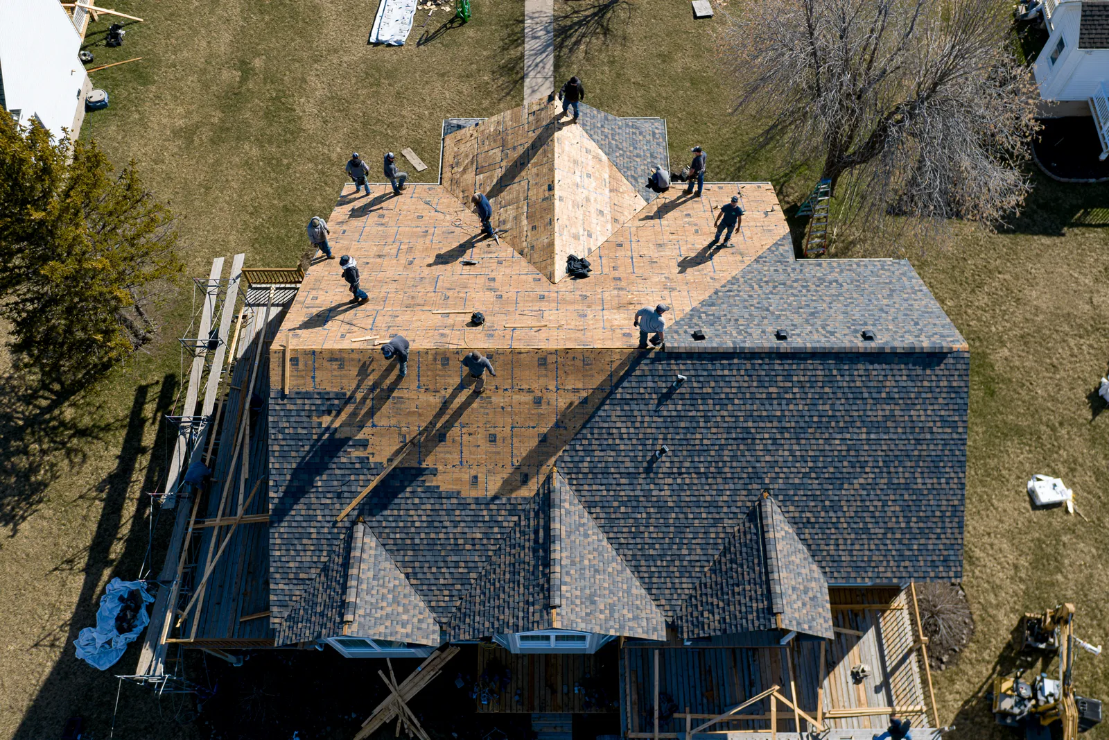 Roofers work across a sprawling multi-gable roof seen from an aerial drone view